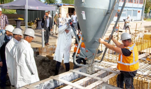 De Leiderdorpse wethouder Willem Joosten opent de kubel waardoor het beton in de bekisting voor de fundering kan stromen.