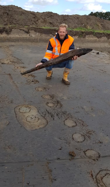 Archeoloog Jeroen Loopik met een stuk houten paal van de Romeinse weg