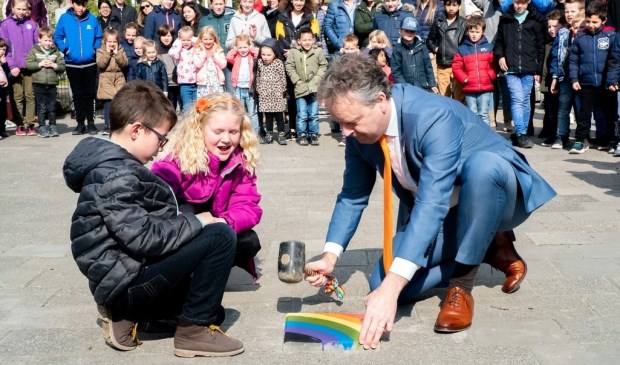 Samen met twee leerlingen legt wethouder Willem Joosten de laatste steen in het vernieuwde plein van PCOB De Regenboog.