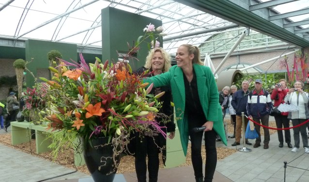 Nicolette Kluijver (rechts) steekt een lelietak in een bloemstuk, daarbij bijgestaan door Stephanie van Erven.