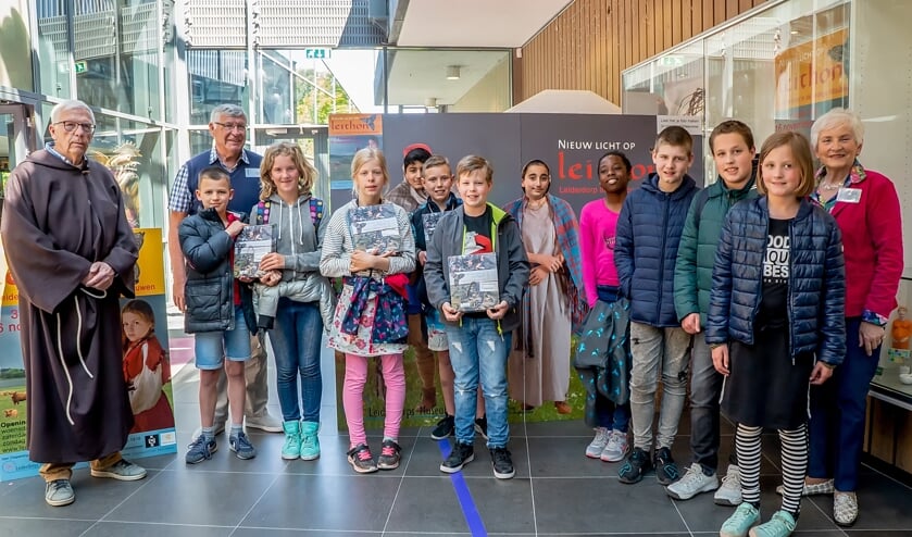 Links museumdirecteur Bob Reidsma, voor de gelegenheid verkleed als middeleeuwse monnik, met twee museummedewerkers en kinderen van de Leiderdorpse basisscholen die de boeken kwamen afhalen.