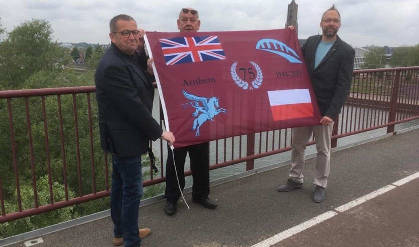 Karl van den Top en Kevin van Guilik overhandigen het eerste exemplaar van de Herdenkingsvlag aan Marcel Legerstee. (foto: Ome Joop's Tour)