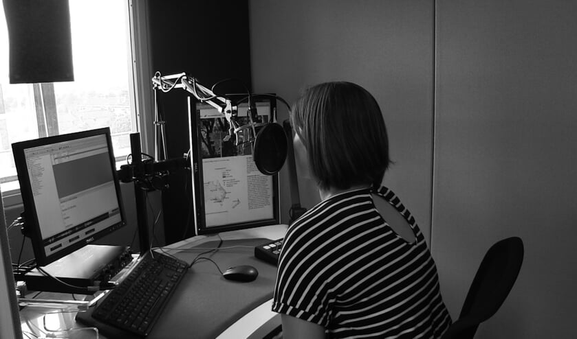 Een vrouw zit in een opnamestudio en leest vanaf een scherm een boek voor (foto: Iris Knuit)